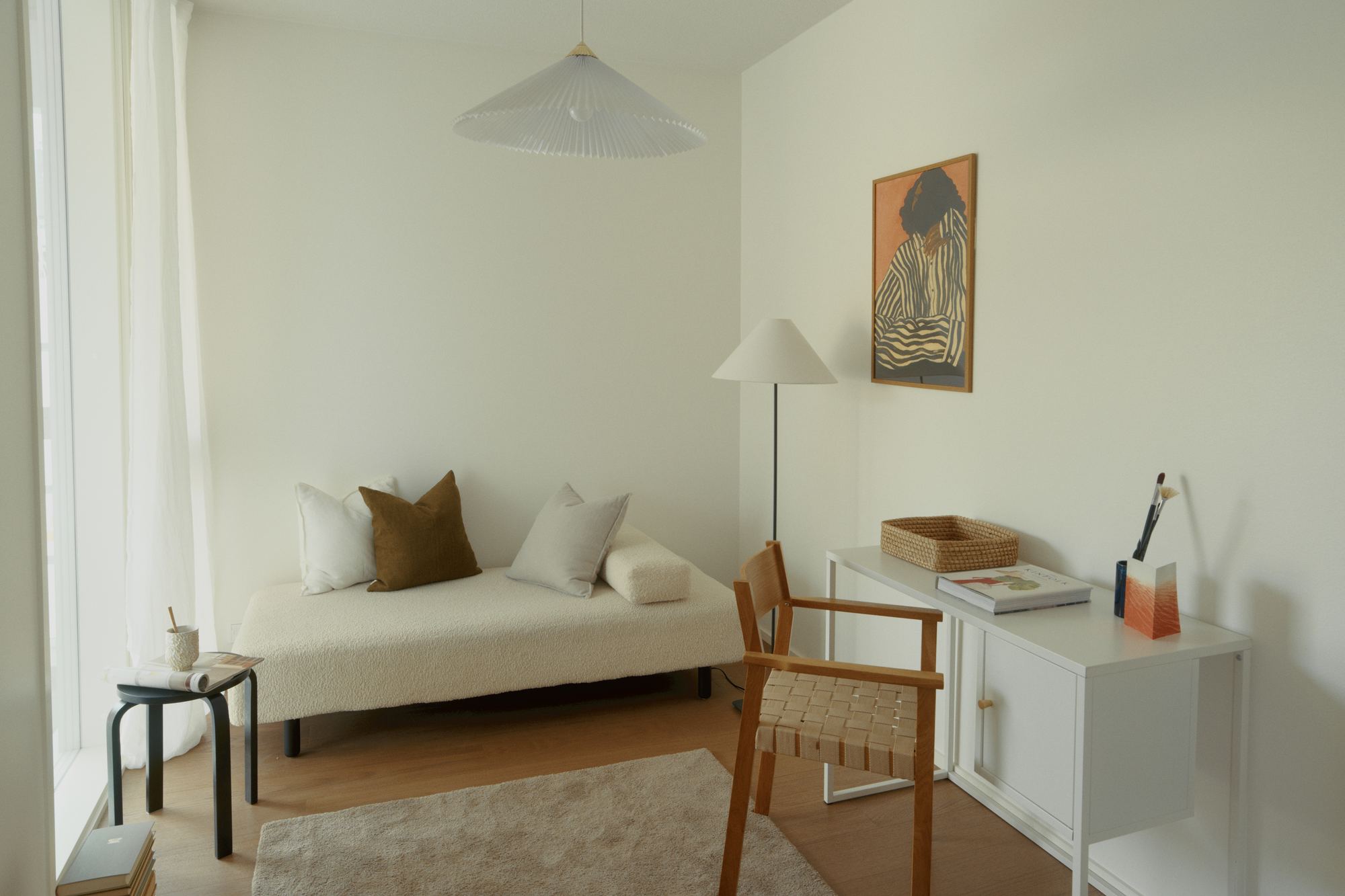 A room with a daybed, a desk and a window glowing through the curtains