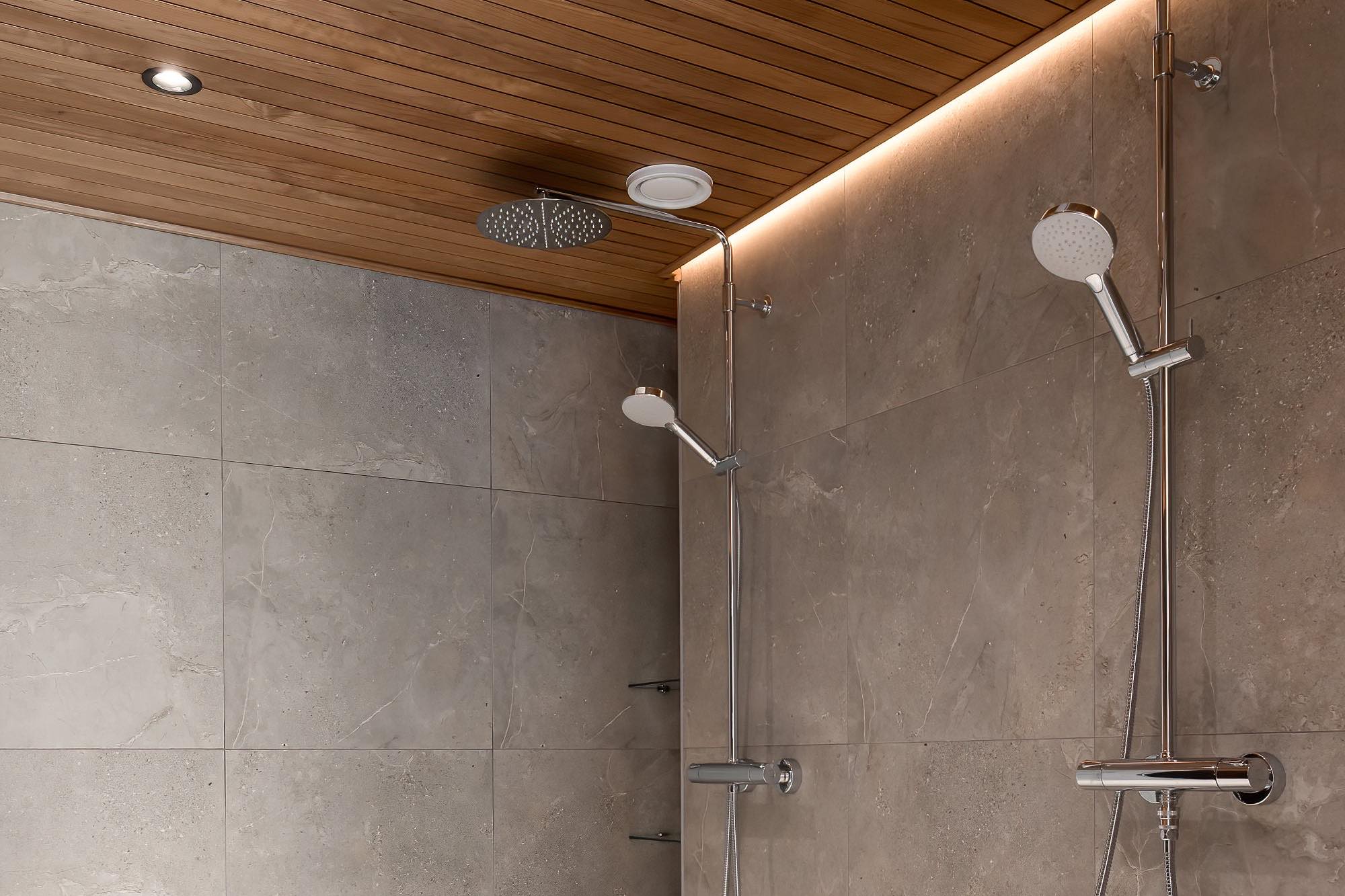A shower room: stone tiles on the walls, a wood-panelled ceiling and a strip of light along its edge