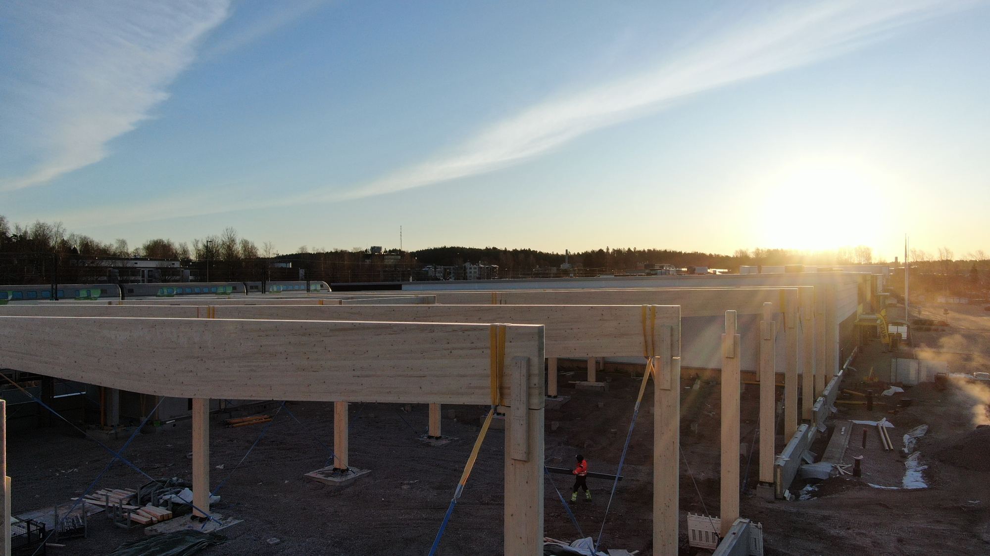 Glulam beams and columns in evening sun on the Kirkkonummen Tähti site, a builder under the beams
