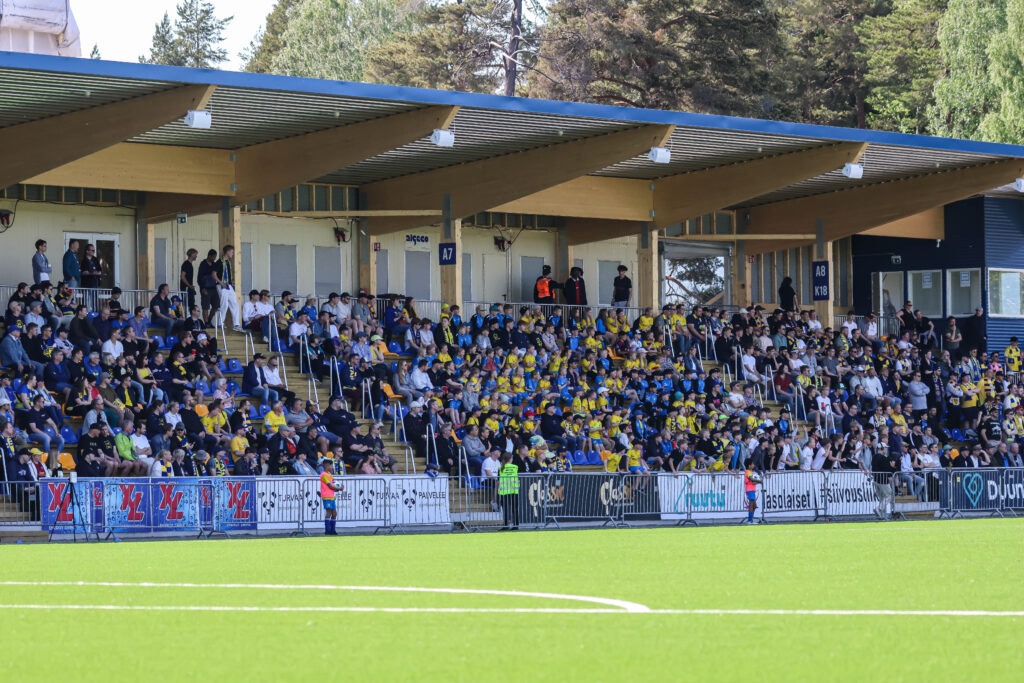 The timber-roofed stand of Oulunkylä stadium full of spectators on a match day